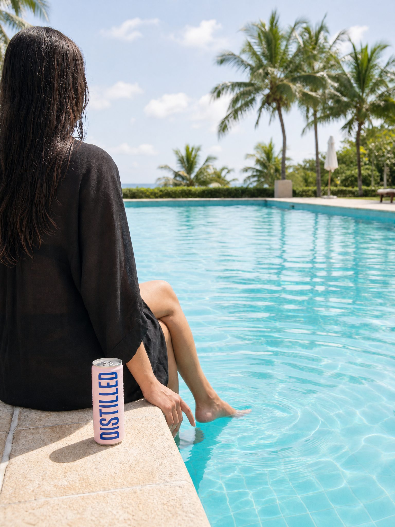 A woman relaxing at the pool edge in bright daylight, the can beside her