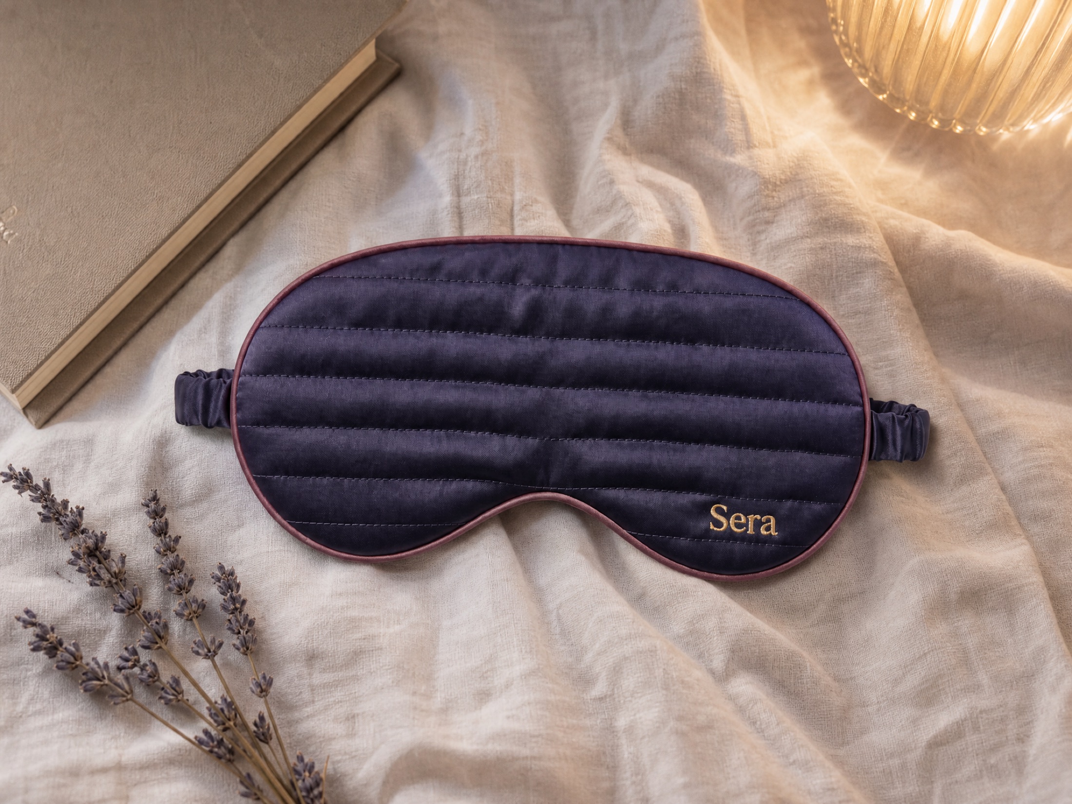 A top-down flatlay of the mask on linen beside a book and dried lavender