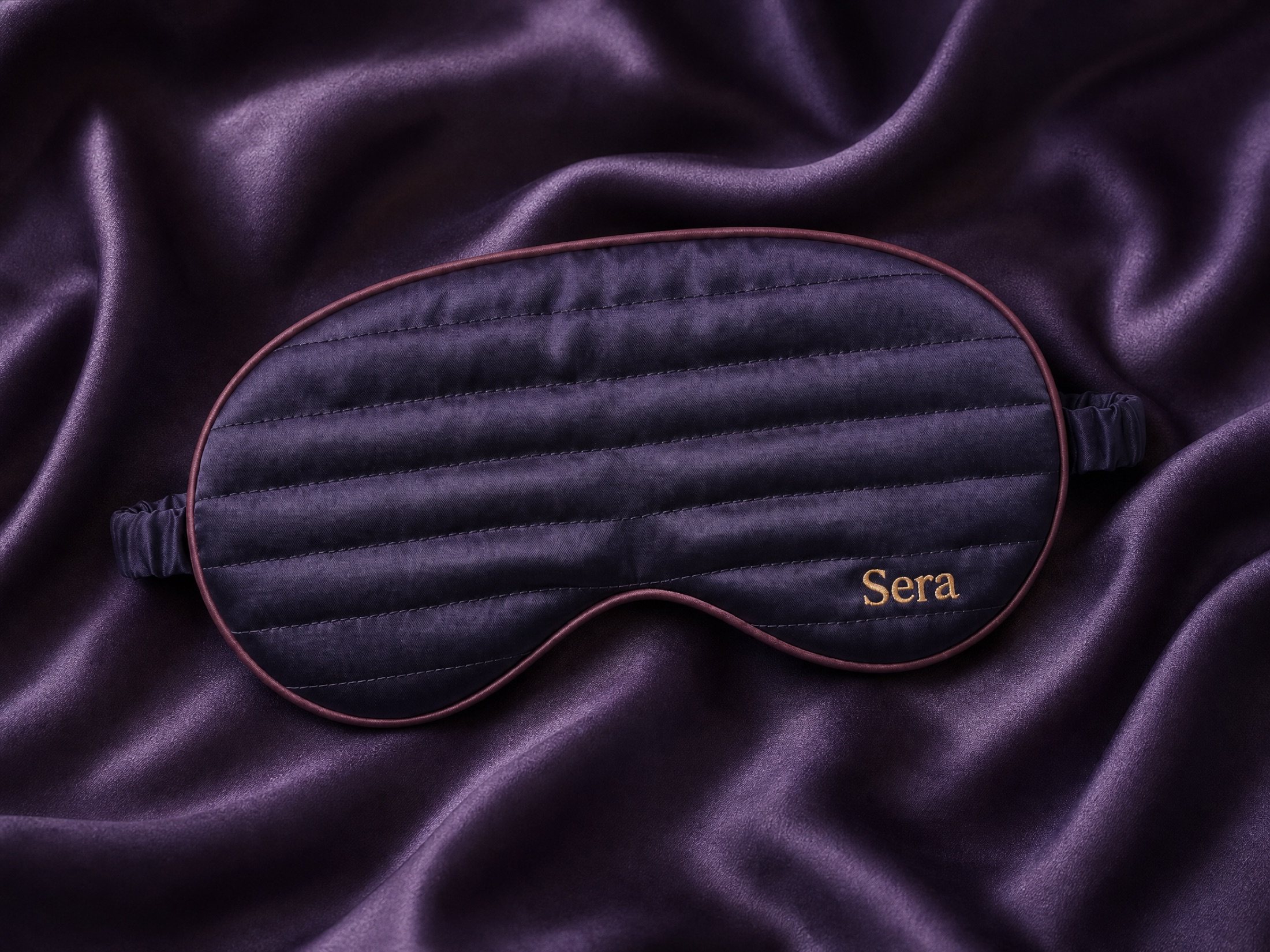 The Sera mask resting on draped deep-violet silk, a pure tactile product shot