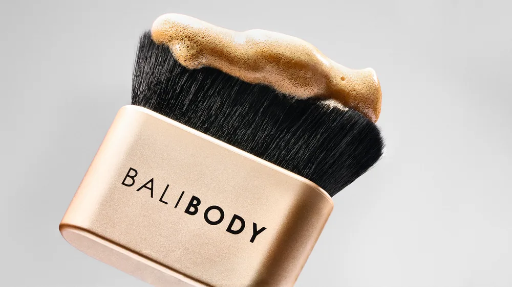 Bali Body gold kabuki brush loaded with bronzer, shot flat on a pale grey surface.