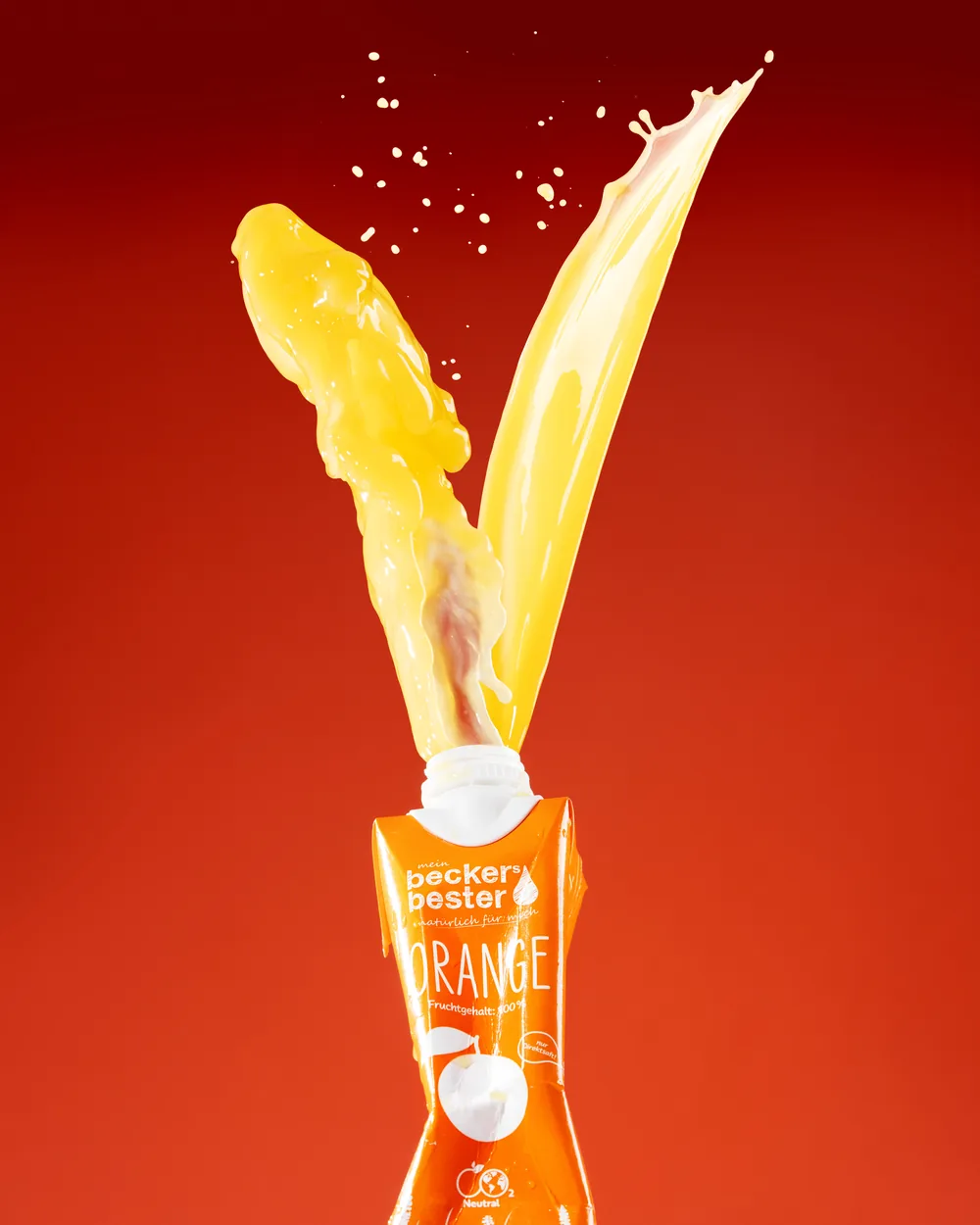 Orange juice arcing out of a becker's bester carton against a deep red background.