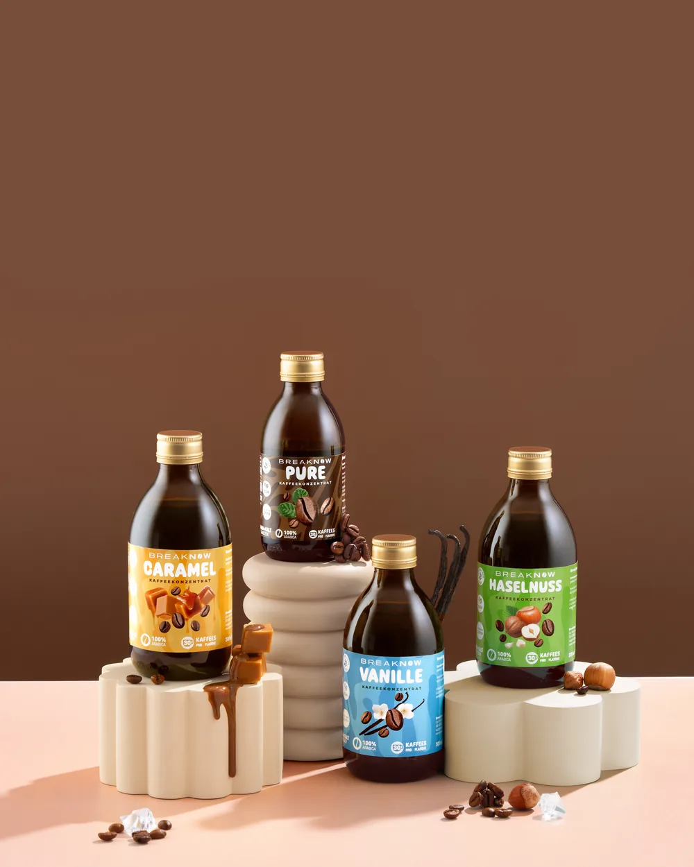 Set of four Breaknow flavoured coffee syrups on stone pedestals with scattered coffee beans.