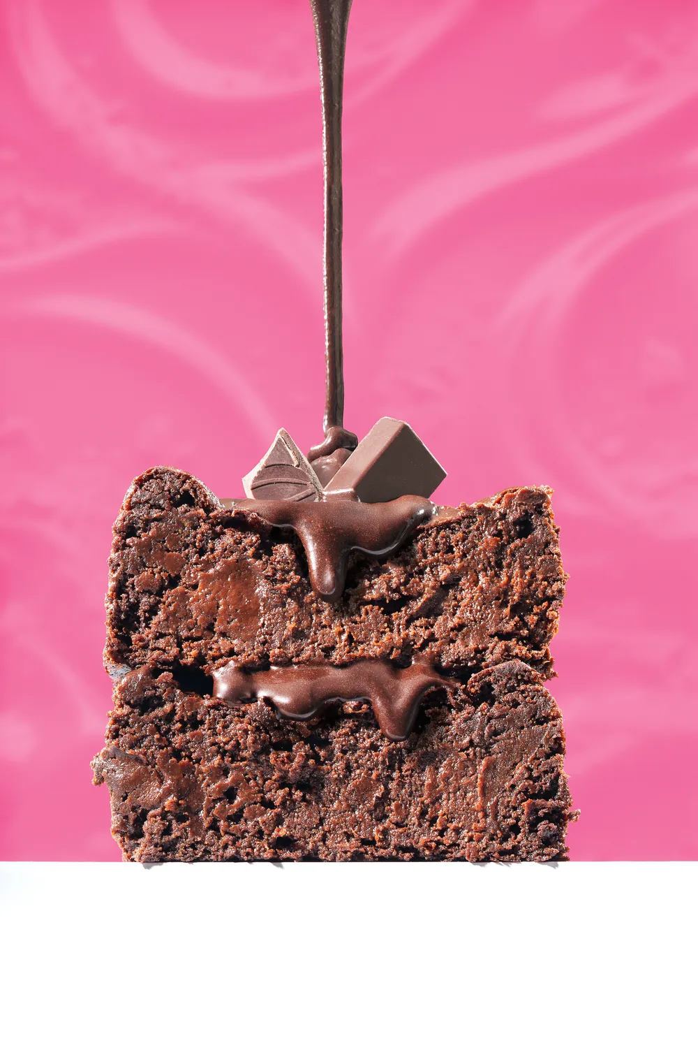 Chocolate brownie stack with melted chocolate poured over it against a pink background.