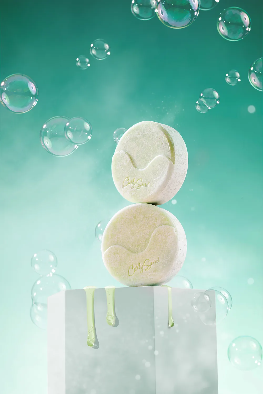 Two stacked round Curly Secret bottles with green product dripping down, bubbles rising on teal.