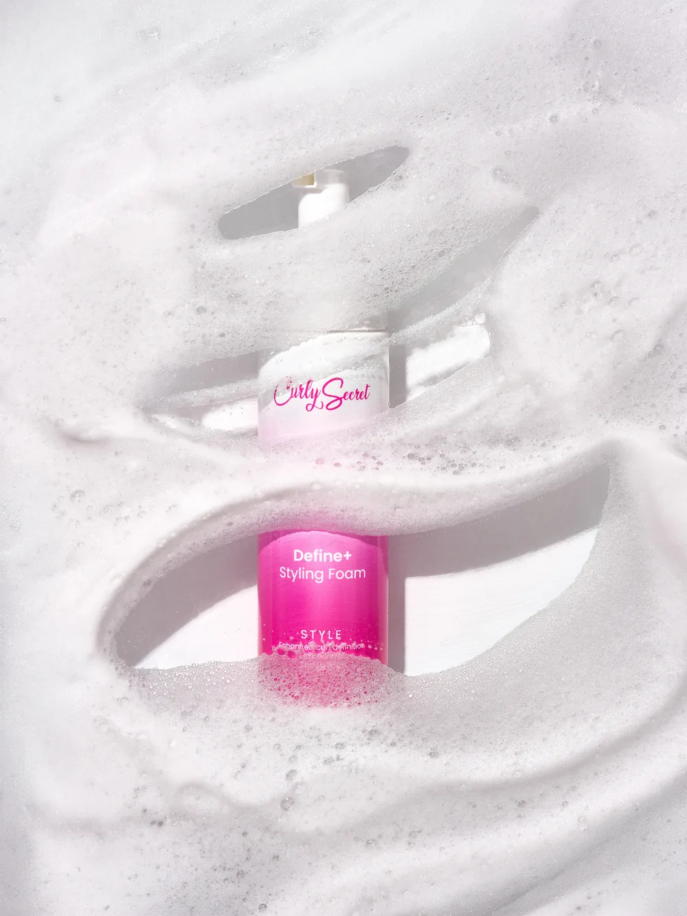Curly Secret styling bottles resting in a bed of white cleansing foam.