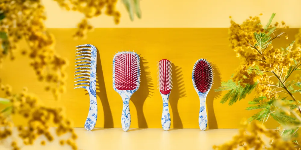 Row of five Denman Blue Belle brushes with floral handles on a yellow background with mimosa.