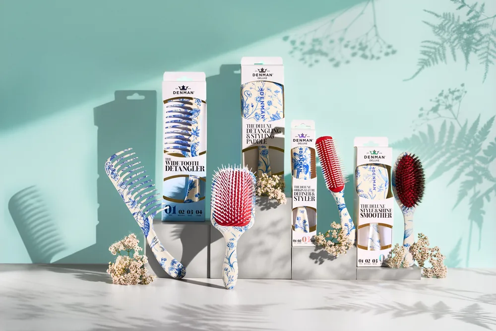 Denman Blue Belle brushes and packaging displayed on a teal background with palm shadows.