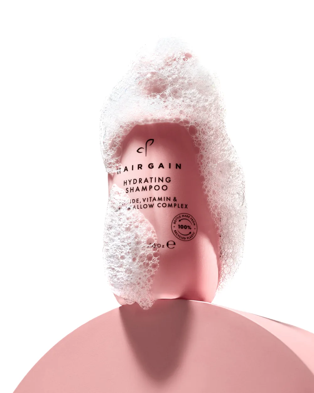 Hairgain hydrating shampoo bottle wrapped in a sculpted crown of foam on a pink background.