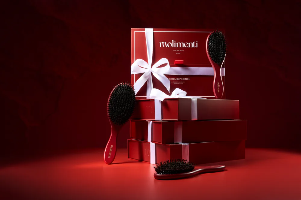 Molimenti gift boxes tied with white ribbon beside hairbrushes on a deep red background.
