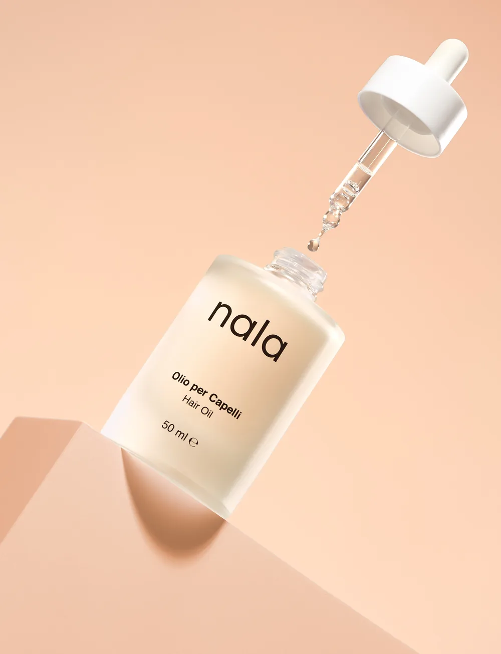 Nala hair oil bottle with its dropper lifted, casting a long shadow on a peach background.