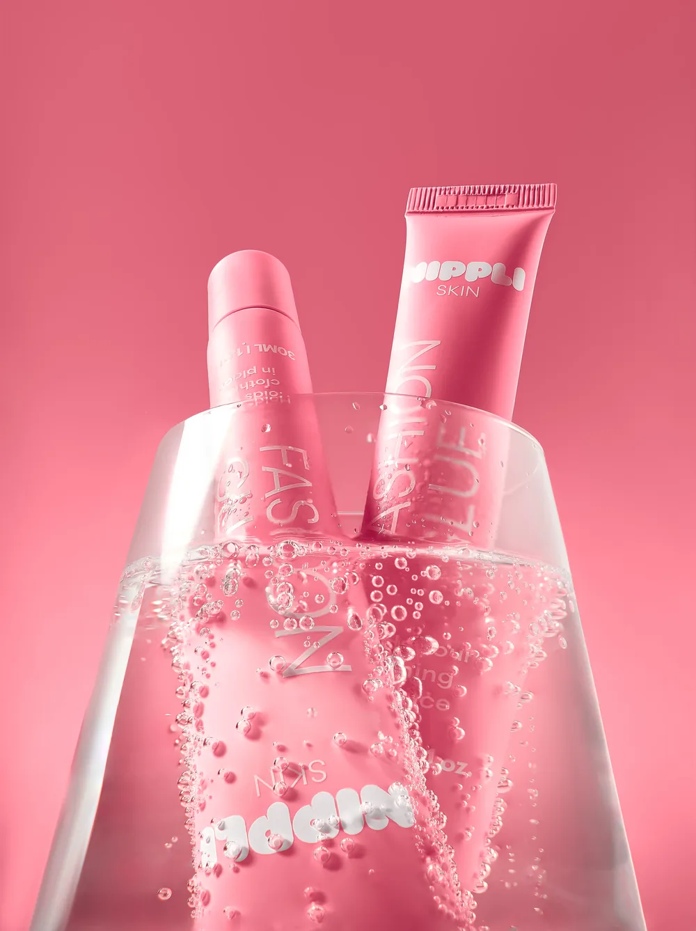 Two pink Nippli tubes half submerged in water with bubbles rising around them.