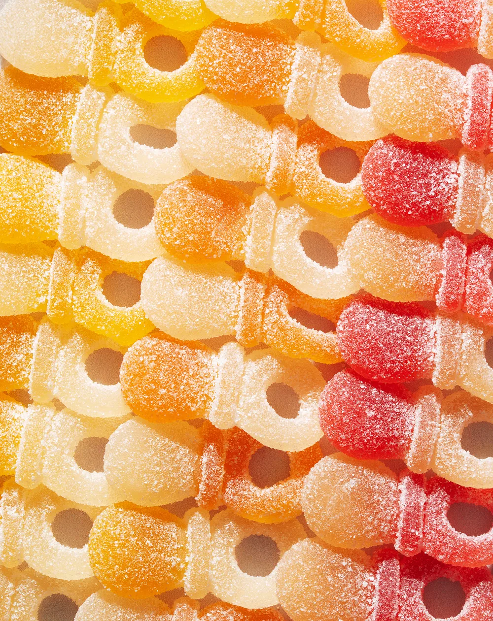 Tight pattern of sugar-coated gummy rings in yellow, orange and red.