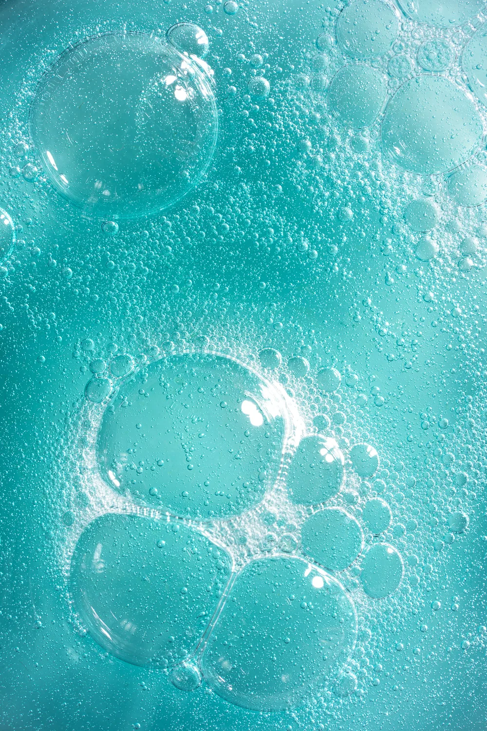 Macro of large bubbles suspended in bright teal liquid.